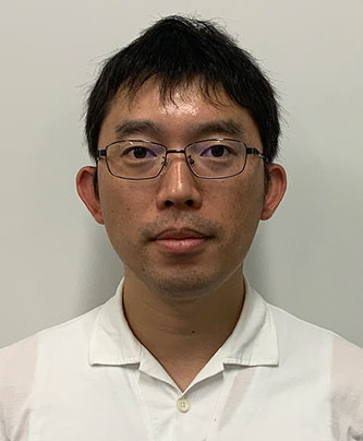 Portrait photograph of a speaker for a Doshishia case study, wearing glasses and a white shirt, in front of a plain background.