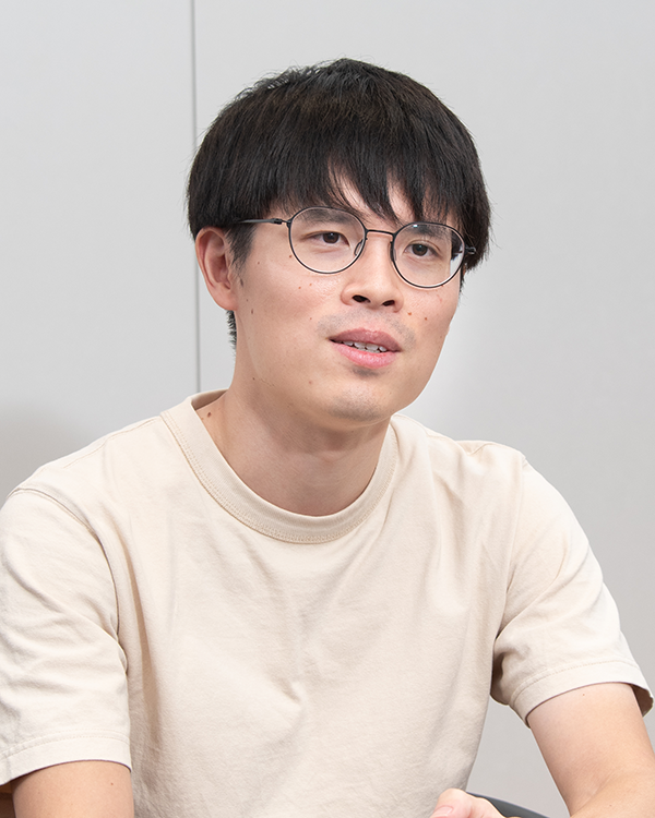 Portrait of a person with short dark hair and glasses, wearing a light-colored shirt, sitting for an interview. This image is used for the Mixi case study on the AWS Japan website.