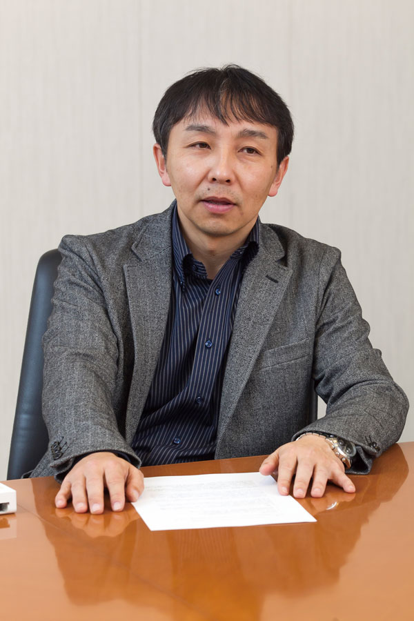 A Panasonic representative in a suit jacket sits at a table with a document, during an interview for AWS solution case studies.
