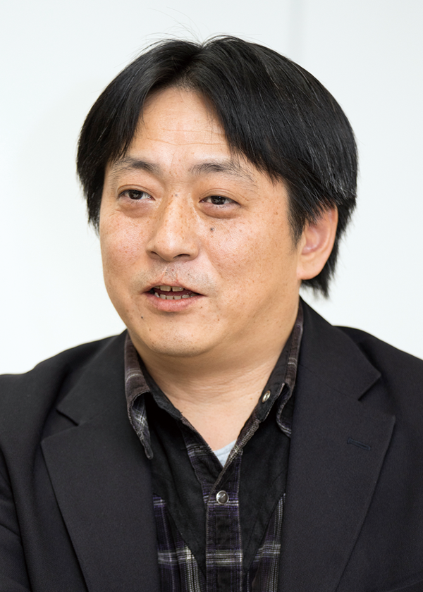 A person wearing a black blazer over a plaid shirt.
