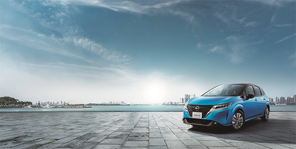 A blue Nissan automobile is parked on a spacious tiled plaza with a city skyline and water in the background, under a bright sky with scattered clouds. This image is used for a Nissan automobile case study.