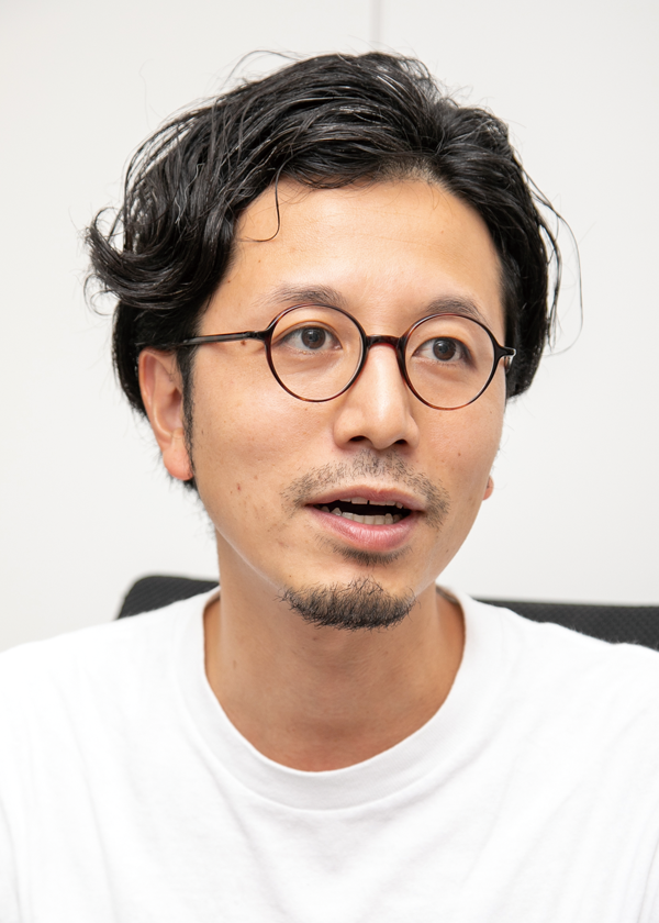 A person wearing a white shirt with dark, wavy hair.