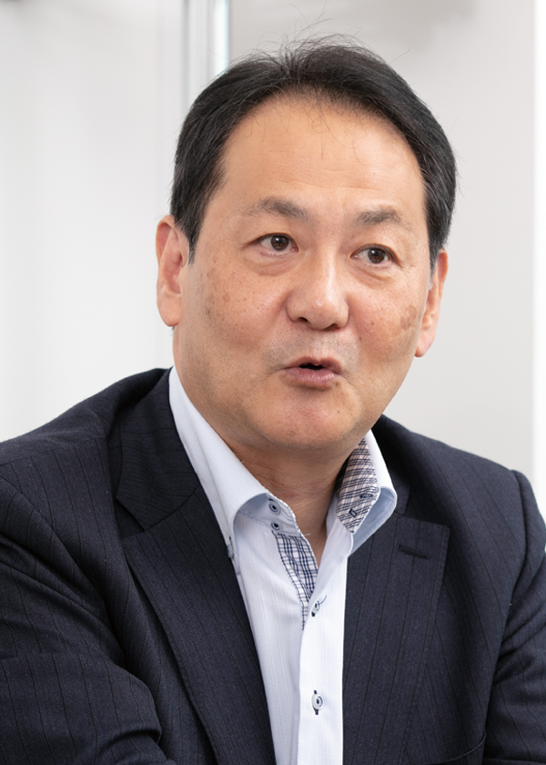 A businessman in a dark suit and light shirt speaking during an interview, featured for DyDo Kasai case study.