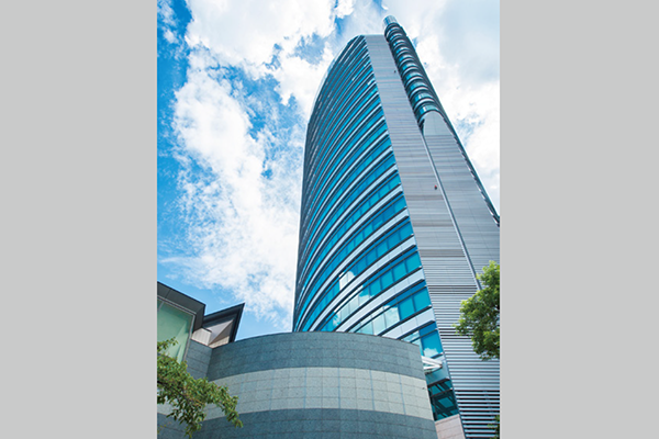 A modern, tall glass and steel office building under a blue sky with clouds, representing Toppan Holdings.