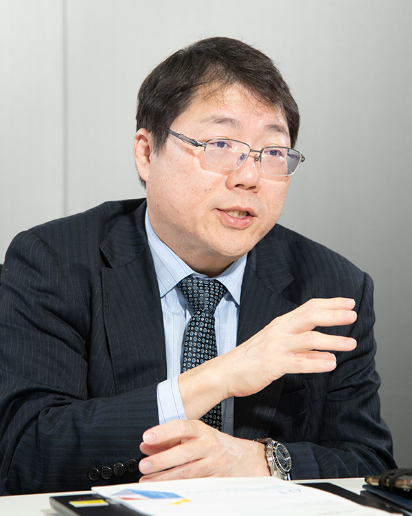 Portrait of a man in a suit and glasses sitting at a table, gesturing with his hand. Used for a Toshiba case study.