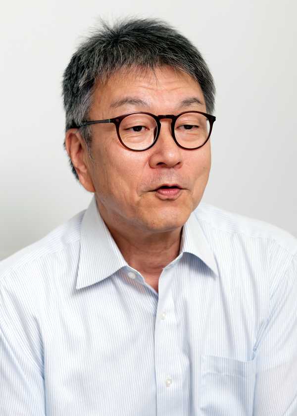 A middle-aged man with short dark hair, wearing round glasses and a light blue striped shirt, pictured against a plain background.