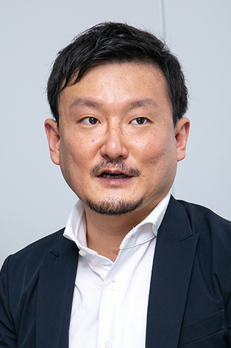 A portrait photograph of a professional man wearing a white shirt and dark blazer, looking slightly to the side, against a plain background.