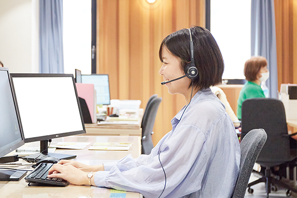A woman wearing a headset works at a computer in a modern office setting. Other workers are visible in the background. This image is used for the Musubu AWS case study.