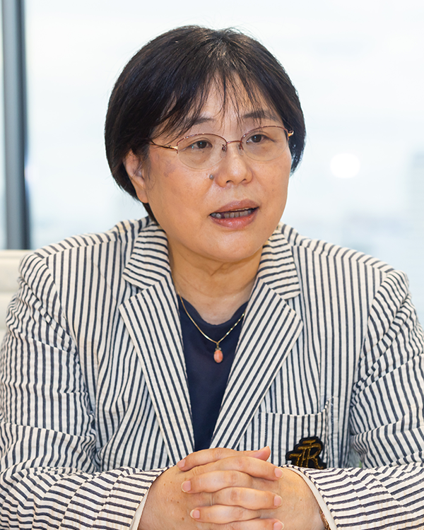 Portrait of an individual in a striped suit jacket, seated at a table during an interview, with hands folded and a light background. Used in Panasonic-related interview or case study content.