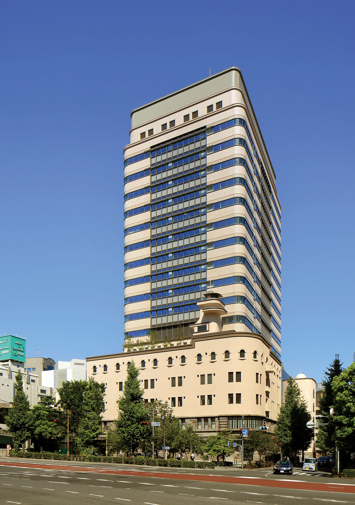 Exterior view of the Mitsubishi Soko office building in Tokyo, showing a modern high-rise structure with glass windows and architectural details, set against a clear blue sky.