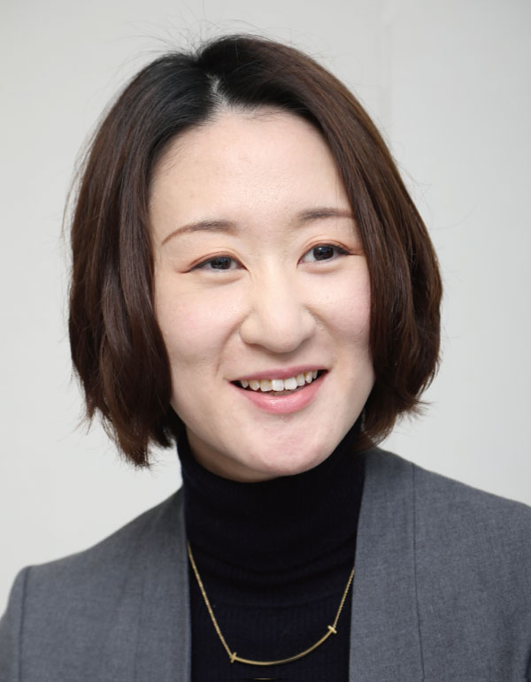 A woman with short hair, wearing business attire and a necklace, smiling in a professional setting.