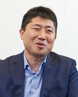 A businessman wearing a blue suit and light blue shirt is smiling during an interview.