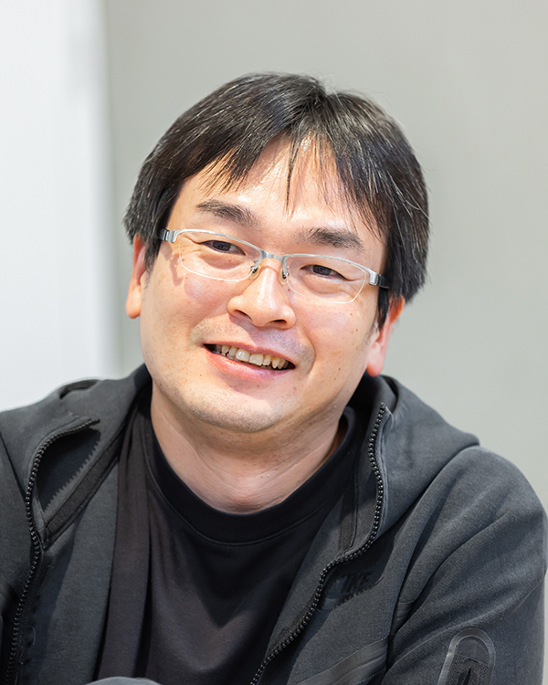 A portrait photo of a man wearing glasses and casual clothing, smiling at the camera.