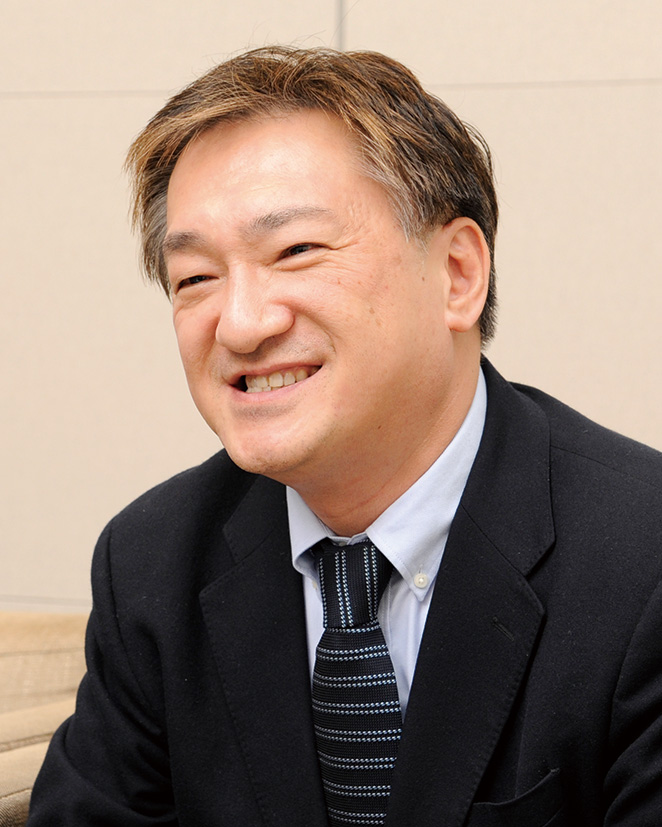 A portrait of a business professional in a suit and tie, smiling, during an interview. Indoor setting with a neutral background.