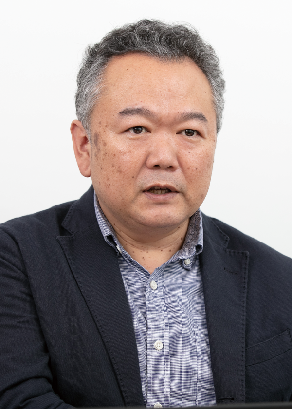 Portrait of a middle-aged man in business attire speaking, set against a light background.