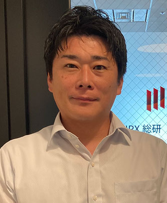 Portrait of a person in a white shirt standing indoors with a patterned glass background featuring office elements and partial text.