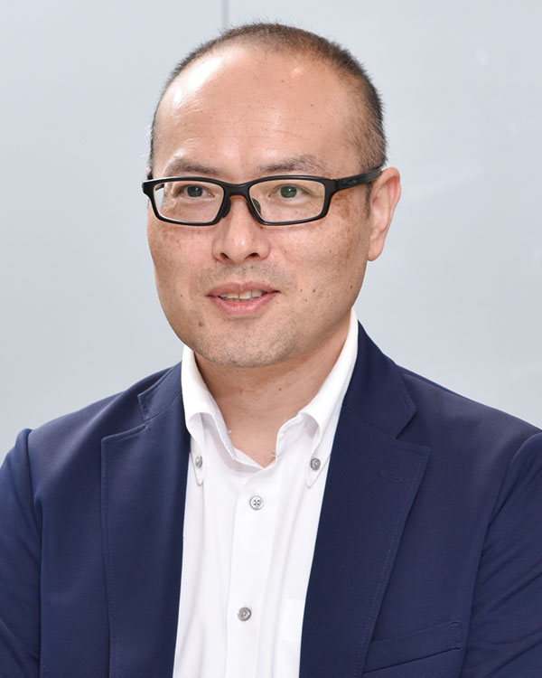 Portrait of a speaker featured in the Mitsubishi Soko case study, wearing glasses and a suit jacket, against a plain light background.
