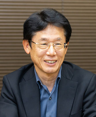 Portrait of Masao Oshimi, a speaker featured in a case study for CRI. He is wearing glasses and a business suit, smiling in front of a neutral background.