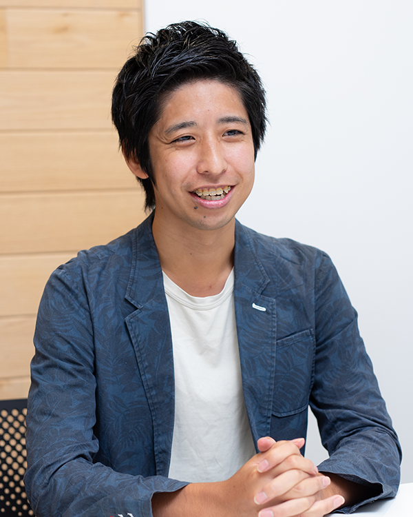 A portrait of a speaker for the Applibot case study, showing a person seated at a desk and smiling, wearing a blue jacket and white shirt.