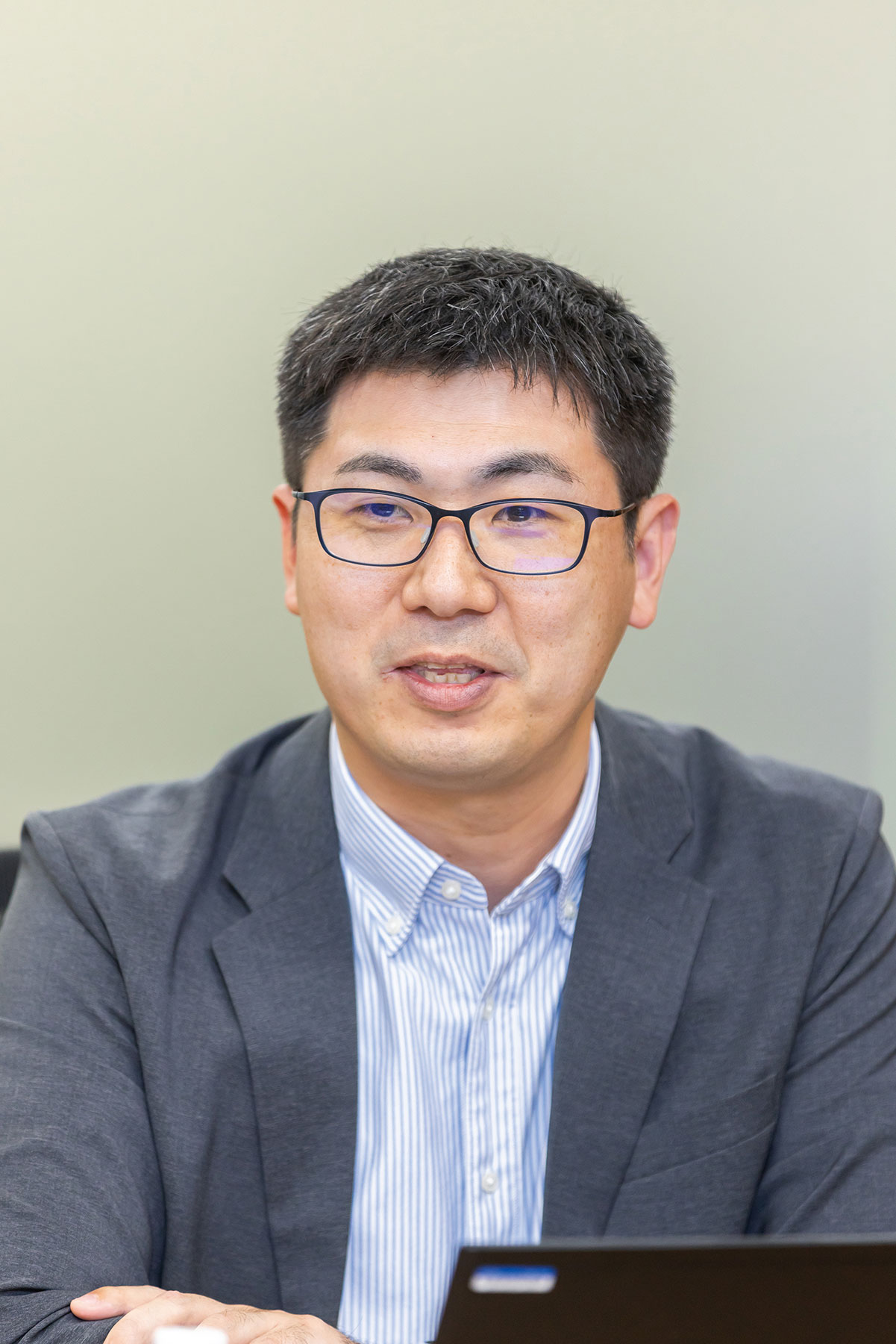 A person wearing glasses and a suit, speaking or presenting, as part of a BIGLOBE case study interview or discussion.