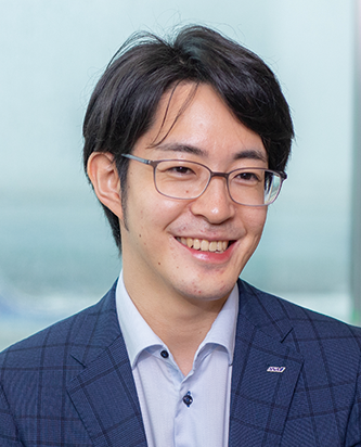 A business portrait of a professional wearing glasses and a blue checkered suit, smiling, with a blurred office background.