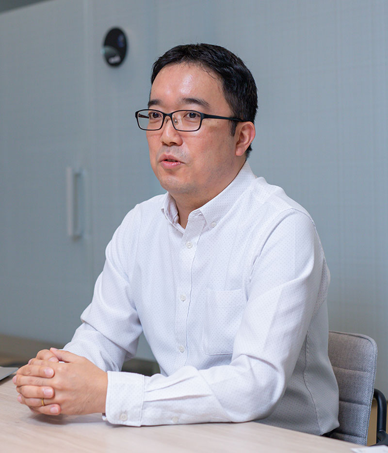 A man in a white shirt and glasses sits at a table speaking, featured as a speaker for the NTT DOCOMO Lemino case study.