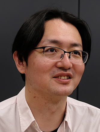 Portrait of a man wearing glasses and a light-colored shirt, set against a dark background.