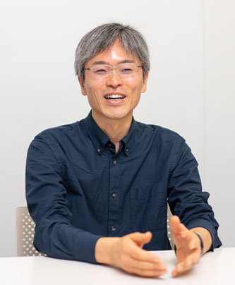 Portrait of a speaker from Sony Interactive Entertainment, wearing glasses and a dark blue shirt, seated at a table and speaking with hands gesturing.