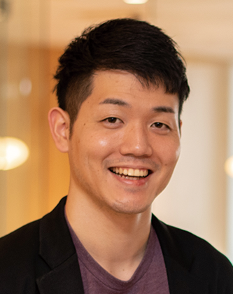 Portrait of a smiling man in business casual attire, indoors with a blurred background.