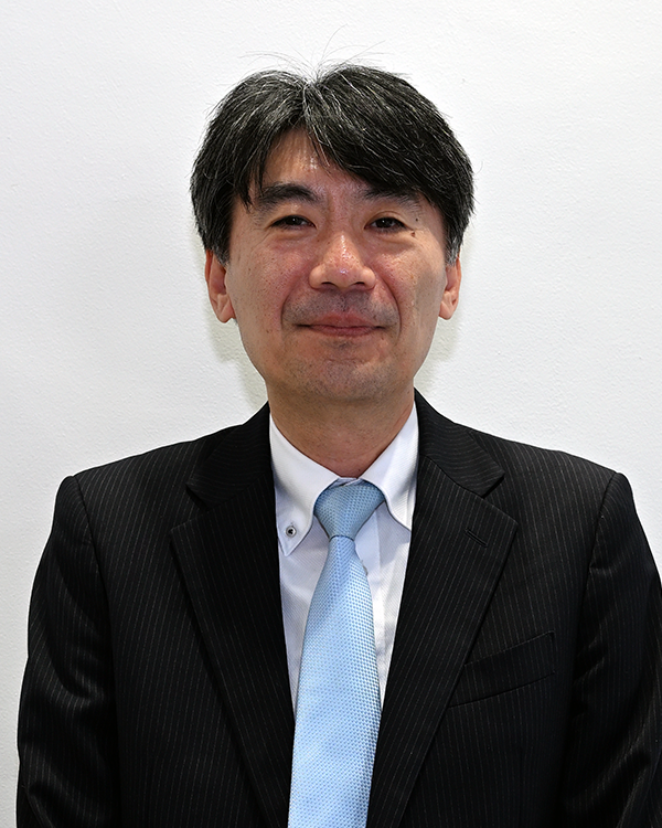 Portrait of a person in a suit with a light blue tie, used for the Fujitsu General case study. The person is standing against a plain white background.