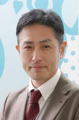 A man in a suit and tie posing for a portrait in front of a blue and white background with circular and heart shapes.