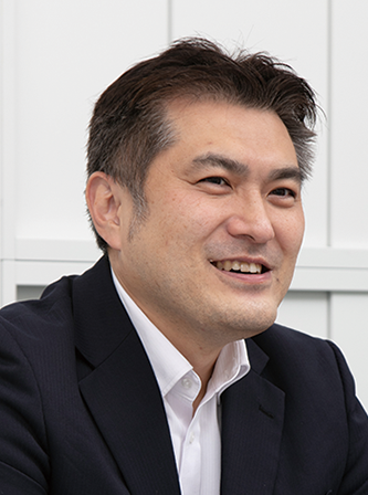 Portrait of an Asian man in a business suit, smiling and looking to the side, against a light background.