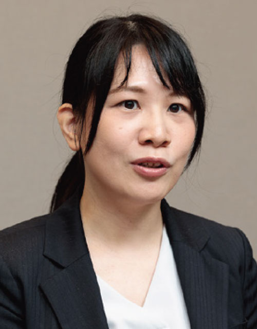 A person wearing a black blazer and white blouse with their hair tied back.