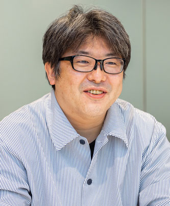 Portrait of Toshiyuki Matsushima, speaker for V-CUBE, wearing glasses and a striped shirt, featured in an AWS Japan solution case study.