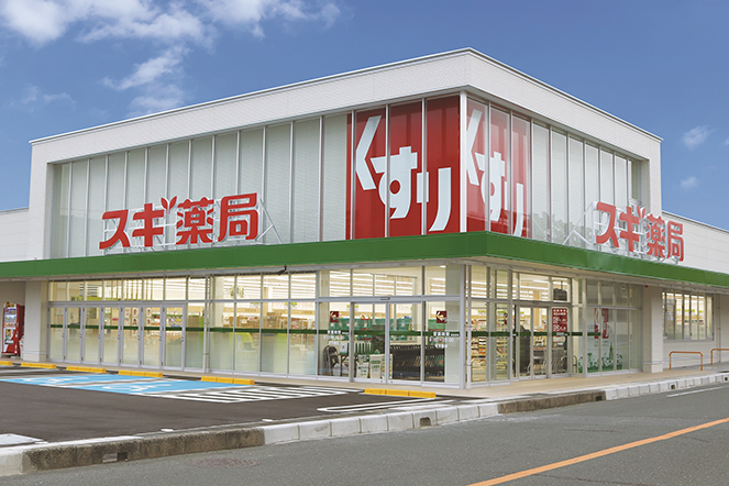 Storefront view of a Sugi Pharmacy (スギ薬局) in Japan, showing large glass windows, signage, and parking spaces in front of the building.