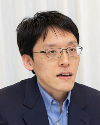 Portrait photo of Mr. Kagaya from Mitsubishi Estate, wearing glasses and a suit, with a neutral background.