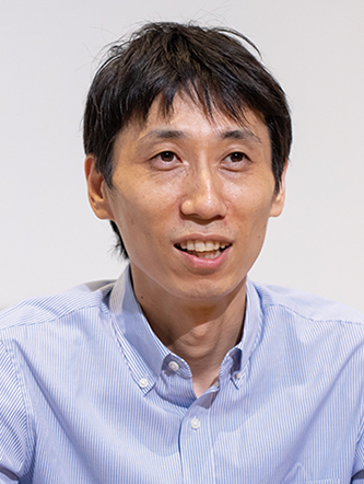 A man with short black hair wearing a light blue button-up shirt, facing forward and smiling slightly.