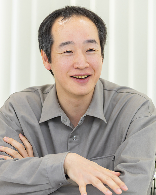 A portrait of a person in a gray shirt, seated and smiling, featured in the ecbeing case study for AWS Japan.