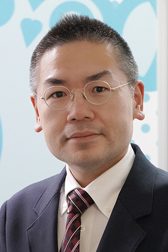 A professional portrait of a man in a suit and tie with glasses, set against a background with heart and circle patterns.