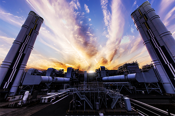 A dramatic view of JERA's power plant with industrial structures and towers silhouetted against a colorful sunset sky.