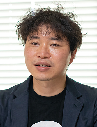 Portrait of Mr. Osano in an interview setting for Desamis, featured in a solution case study. A man with dark hair is pictured wearing a dark jacket in front of window blinds.