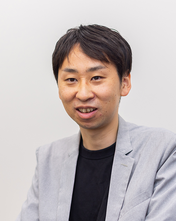 Portrait of a man in a light gray jacket and black shirt, photographed in front of a plain light background.