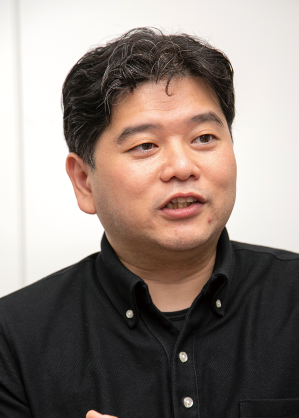 A portrait photo of a person wearing a black button-up shirt, pictured against a plain background.