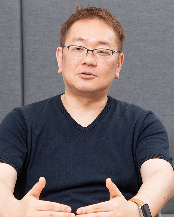 Portrait of a man with glasses in a dark shirt, sitting in front of a gray background. This image is used for the ExaWizards case study.