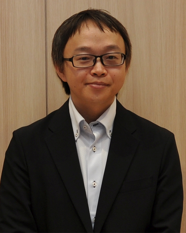A portrait of a person in business attire wearing glasses, photographed against a light wood background, used for the Toppan case study on the AWS Japan website.