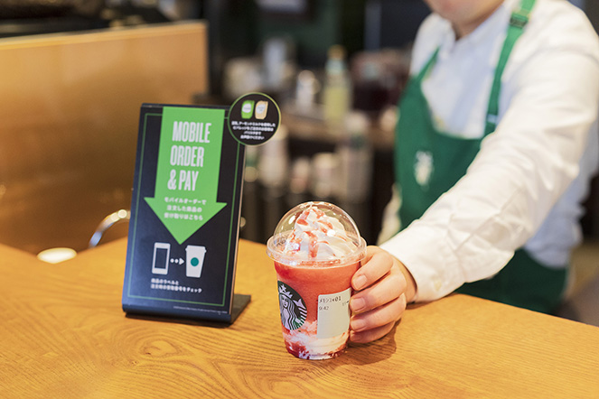 A Starbucks employee hands a colorful drink to a customer at the counter next to a sign promoting the 'Mobile Order & Pay' service.