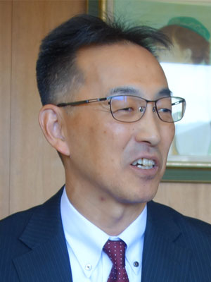 A person wearing a suit and tie in front of a wooden wall and framed artwork.