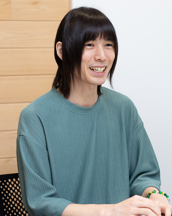 A person sitting and smiling, featured as a speaker for the Applibot case study. The individual is dressed in a teal shirt, seated indoors with a wooden and white background.