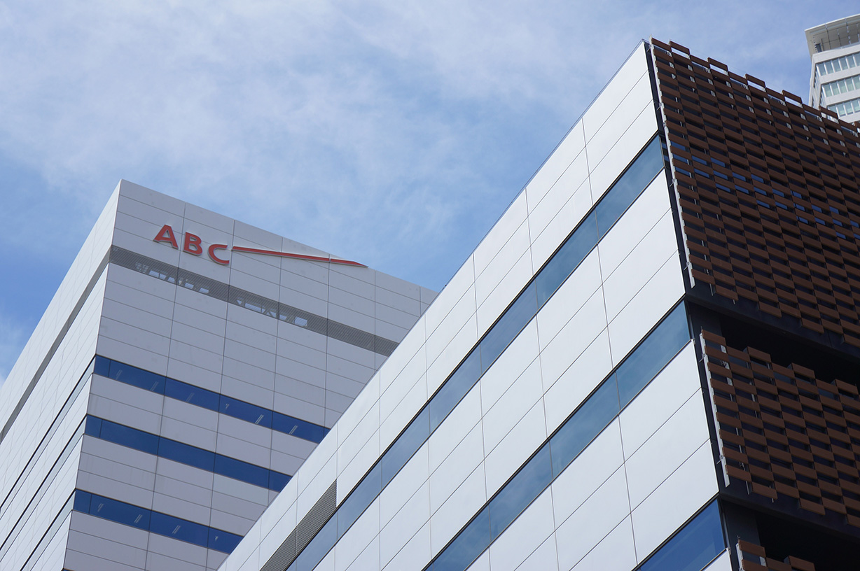 A modern office building with reflective glass and metal panels, featuring the 'ABC' logo at the top against a blue sky.