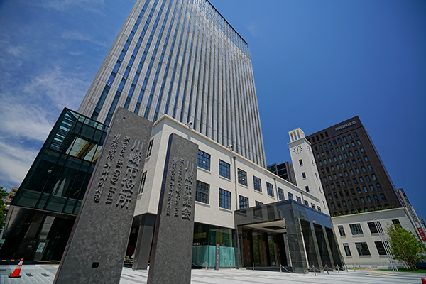Modern office buildings with a tall skyscraper, a clock tower, and stone signposts in the foreground under a clear blue sky.
